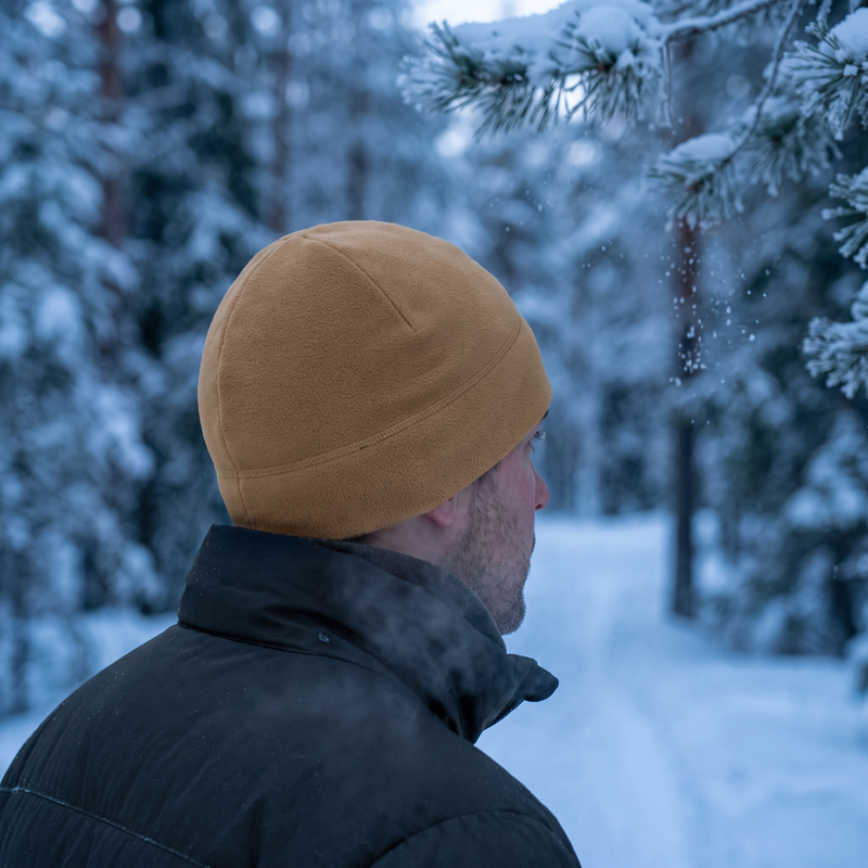 Man on a snowy forest trail wearing the khaki fleece tactical beanie