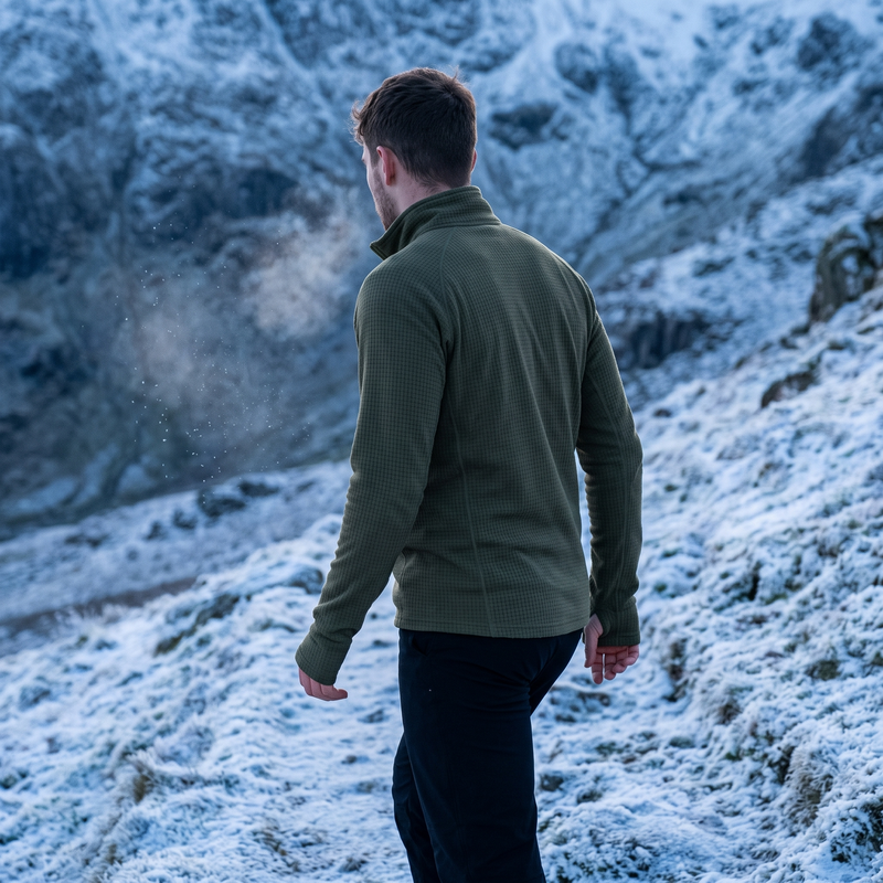 Man on a snowy mountain path in the army green grid fleece base layer top