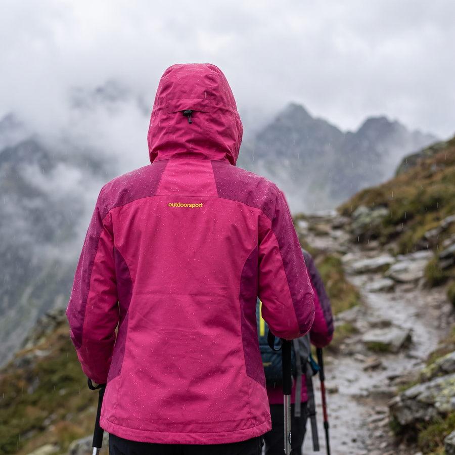 Woman wearing pink waterproof hiking jacket on misty mountain trail